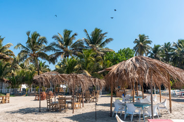Obraz na płótnie Canvas Tropical Palm Paradise. Recreation Relax lounge zone on a sandy beach. Cafe Restaurant on the coast. Sheds made of palm leaves for tourists, tables and chairs. 