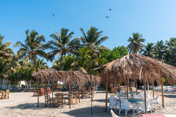 Tropical Palm Paradise. Recreation Relax lounge zone on a sandy beach. Cafe Restaurant on the coast. Sheds made of palm leaves for tourists, tables and chairs. 