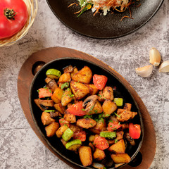 Delicious oven-baked potatoes with herbs and vegetables in a pan, rustic style. Potatoes fried, red cherry tomato, zucchini, onion on gray stone background.
