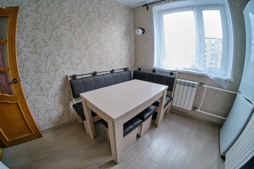 Kitchen corner with a table with a sofa and stools, fisheye. White radiator, beige wallpaper with flowers and window