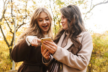 Naklejka premium Two cheerful young pretty girls wearing coats walking together