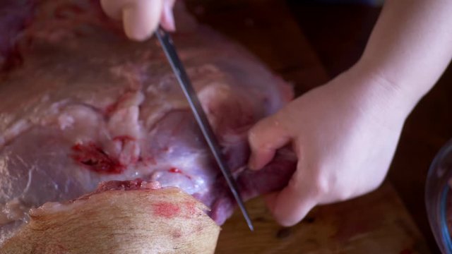 beautiful mature woman in pink sweater and gray economic apron cuts large piece of pork into pieces with knife and ax. girl puts small pieces in meat grinder and grinds them into minced meat
