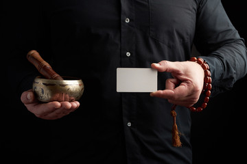 adult man in black clothes holds in his hands a copper singing bowl, object for religious rituals,...