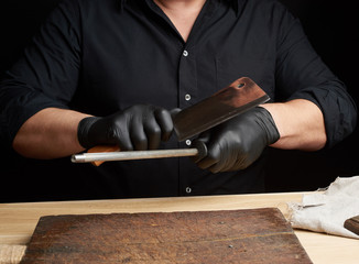 chef in a black shirt and black latex gloves sharpen a kitchen knife