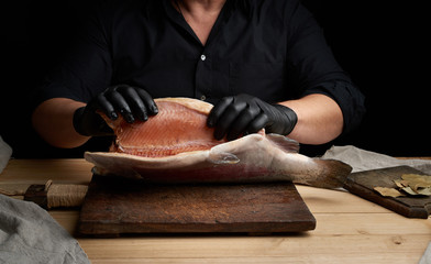 chef in a black shirt and black latex gloves holds a raw carcass of headless salmon fish