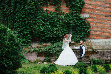 Newly wed couple posing in front of the brick wall of an old noble house overgrown with wild...