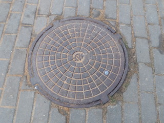 Cast iron manhole cover on the sidewalk made of tiles in the city