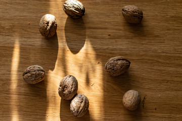  Solid and embossed brown-shelled walnuts lie on a wooden table, illuminated by the harsh sunlight