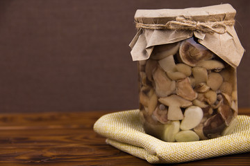 canned fermented mushrooms in a jar garlic bay leaf black pepper stands on a piece of burlap on a brown wooden background