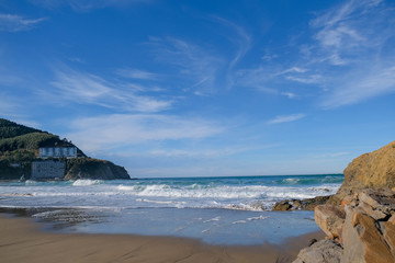 Beautiful urban sandy beach on the ocean on bright sunny day. Amazing blue sky with light clouds. Big waves roll ashore. The Spanish coast of the Atlantic Ocean in winter. Bay of Biscay, Bakio beach.