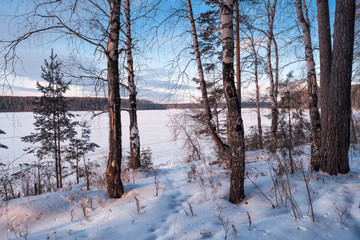 Winter landscape at sunset by a snowy forest lake. Winter forest.