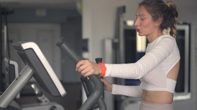 Woman in white sport suite running on fitness machine at the club