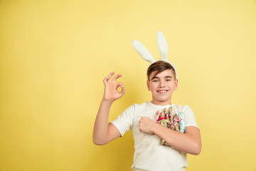 Naklejka premium Showing nice. Decorating. Caucasian boy as an Easter bunny on yellow studio background. Happy easter greetings. Beautiful male model. Concept of human emotions, facial expression, holidays. Copyspace.