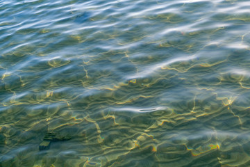 Clear sea water with sun glare in shallow and sandy bottom. Beautiful sun rays are reflected from the surface of the water.