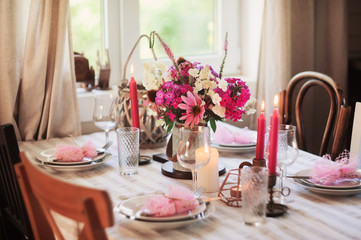 summer festive table setting in beautiful country house. Table decorated with pink flowers and candles.