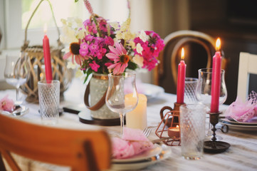 summer festive table setting in beautiful country house. Table decorated with pink flowers and candles.