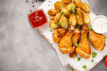 Fried chicken legs with baked potatoes, crispy skin, golden crust. Tomato and white sauces, spices. Delicious homemade food