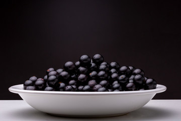 Close up of a food plate with fresh shiny reddish-black Jaboticaba berry fruit lit from above against a dark background