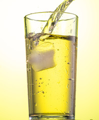 yellow carbonated lemonade in a glass with ice, flow and splash