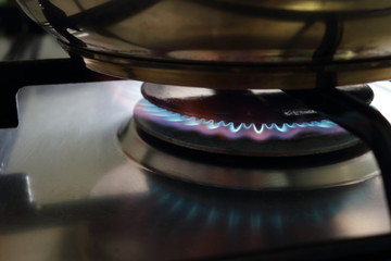 Cooker (household, home, domestic appliance) on propane butane (liquefied or liquid petroleum gas) burn with blue flame and on grille is metal pot from dishware.