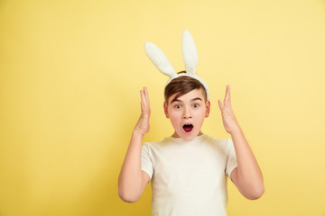Shocked, astonished, wondered. Caucasian boy as an Easter bunny on yellow background. Happy easter greetings. Beautiful male model. Concept of human emotions, facial expression, holidays. Copyspace.