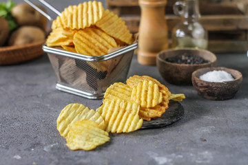 Photo of potato chips on the table with ingredients around. Raw potato tomato. Salt black pepper. On a wooden table. Retro background. On dark board. Studio photography. Image