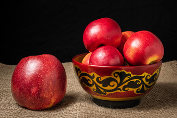 Fototapeta na wymiar Red apples lie in a wooden bowl. A bowl stands on a table covered in burlap.