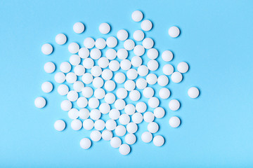 Scattered white pills on a blue background. Medical, pharmacy and healthcare concept.