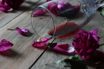 fallen glass of red wine against a background of scattered faded roses