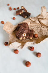 Pieces of milk chocolate with hazelnuts randomly lie on beige mashed craft paper