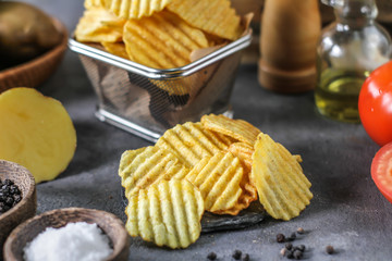 Photo of potato chips on the table with ingredients around. Raw potato tomato. Salt black pepper. On a wooden table. Retro background. On dark board. Studio photography. Image
