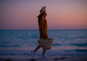 woman with beach bag walking on beach at sunset