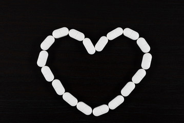 Obraz premium Pills over black background. Heart shape made of pills.