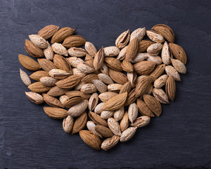 Variety of almonds, mountain and garden, out in shape of heart on black slate background. top view