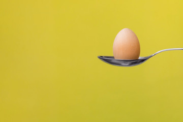 Egg on a spoon on a mustard background. Easter composition, copy space, flat lay, food.