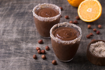 Chocolate mousse with cream, hazelnuts and orange in glasses on an old dark wooden table