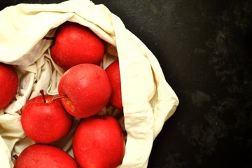 Red apples in a cloth bag. Apples on a dark background in a cotton, linen bag. View from above.