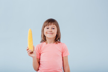 smiling girl has a corn in her hand. isolated on blue background, copy space, in studio, profile view - obrazy, fototapety, plakaty