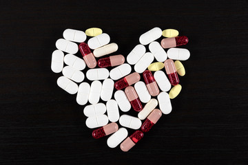Pills over black background. Heart shape made of pills.