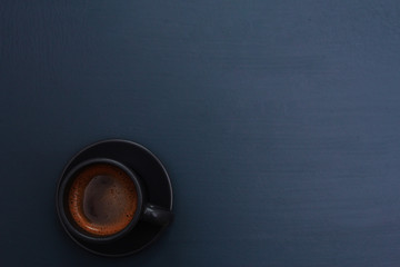 Dark grey cup of coffee on blue table. Hot drink concept. Coffee shop, espresso, top view, copy space