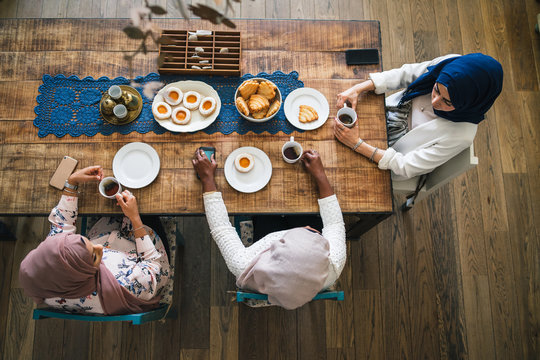 Three Young Muslim Women Drinking Tea At The Kitchen Table - Arabian Millennials At A Time Of Relaxation At Home - Top View