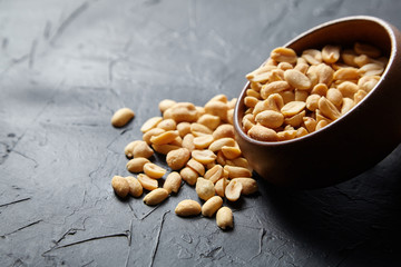 Salty beer snack in round wooden bowl with roasted peeled peanuts on dark background