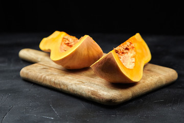 Butternut squash pieces with seeds on wooden cutting board on black background, closeup. Pumpkin seeds. Cooking winter squash