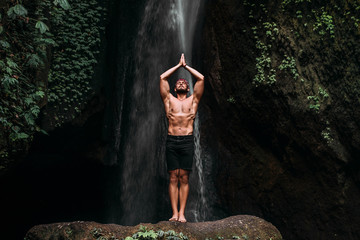 A man of athletic build does yoga. Healthy lifestyle. The concentration of the body. A man does yoga in nature. A man does yoga in Bali. A man meditates in nature. Meditation at the waterfall