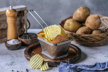 Photo of potato chips with raw potato on wooden table. Front view potato chips. Dark background. Retro style. Homemade. American snack. Junk food. Still life. Image
