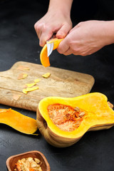 Butternut squash, woman peeling a pumpkin. Female hands with steel knife, wooden cutting board on black background. Cooking sweet winter squash