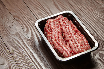 Ground beef in a black plastic tray on wooden table. Uncooked mincemeat. Forcemeat, fresh raw minced meat