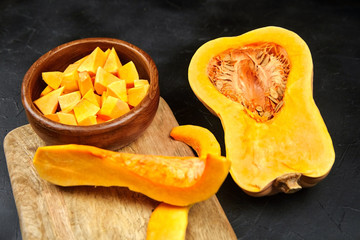 Butternut squash pieces, wooden bowl with pumpkin seeds, cutting board on black background, closeup. Cooking winter squash