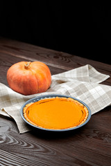 Thanksgiving pumpkin pie in baking tray, squash, kitchen towel on brown wooden table