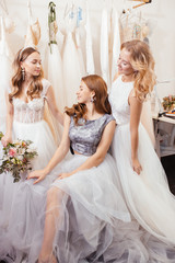 portrait of three beautiful brides or fiancee posing at camera together, wearing white wedding dresses, attractive romantic girls in wedding salon